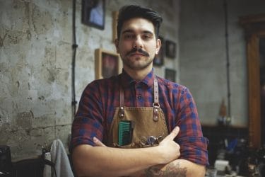 barbier met armen over elkaar en kappers benodigdheden in zijn schort