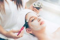 vrouw krijgt een gezichtsmasker aangebracht met kwast in beauty salon