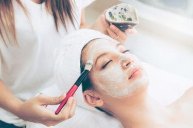 vrouw krijgt een gezichtsmasker aangebracht met kwast in beauty salon