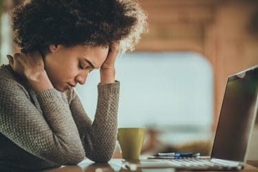 vrouw achter een computer met hoofdpijn en nekpijn