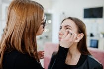 Visagiste brengt make-up aan bij jonge vrouw