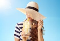 vrouw met cocktail verbergt haar witte huid onder grote zonnehoed