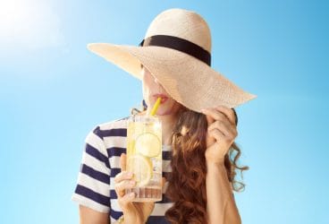 vrouw met cocktail verbergt haar witte huid onder grote zonnehoed